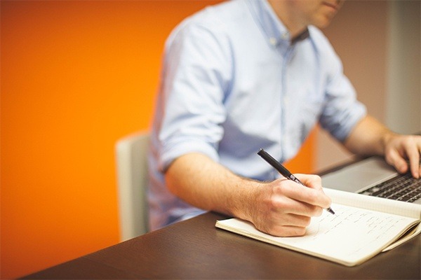 A legal expert in a blue shirt focused on drafting documents while working on a laptop in a private office with vibrant orange walls, symbolizing the energy and concentration available in a dedicated lawyer's coworking space.