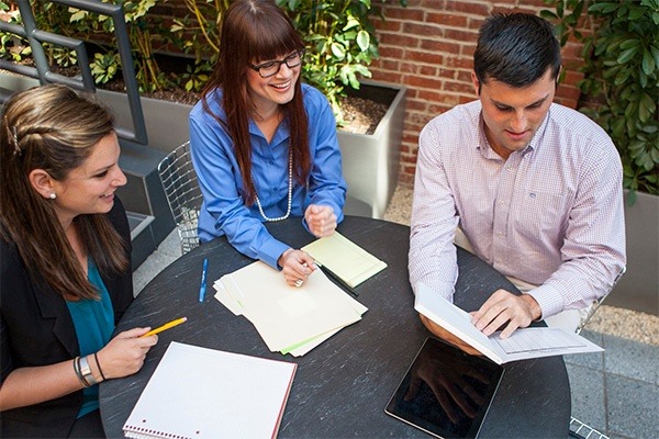 Enthusiastic team of lawyers collaborating on a case in a sunny outdoor terrace area of a modern coworking space, illustrating the dynamic work environments available for legal practitioners.