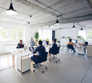 Male and female professionals working in flexible office spaces. Business executives are discussing while sitting by desk at creative workplace. They are in casuals.