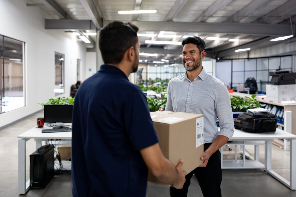 Happy businessman sending a package using a currier service from his office - Mail handling